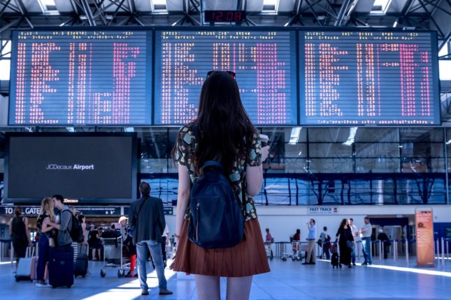 Una ragazza attende davanti al tabellone orario di un areoporto